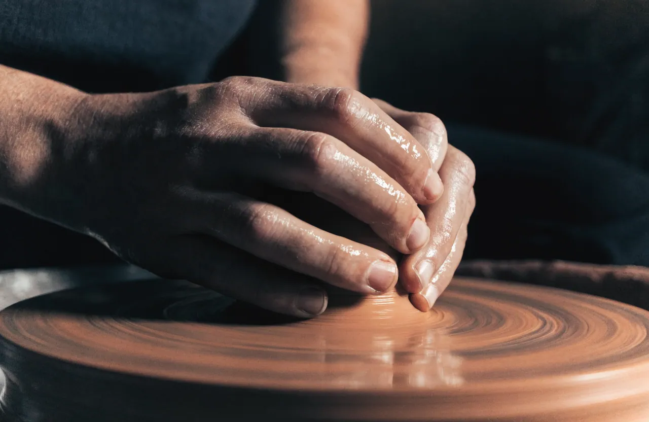 Les mains de la potière au tour, en train de creuser la paroi d'un bol